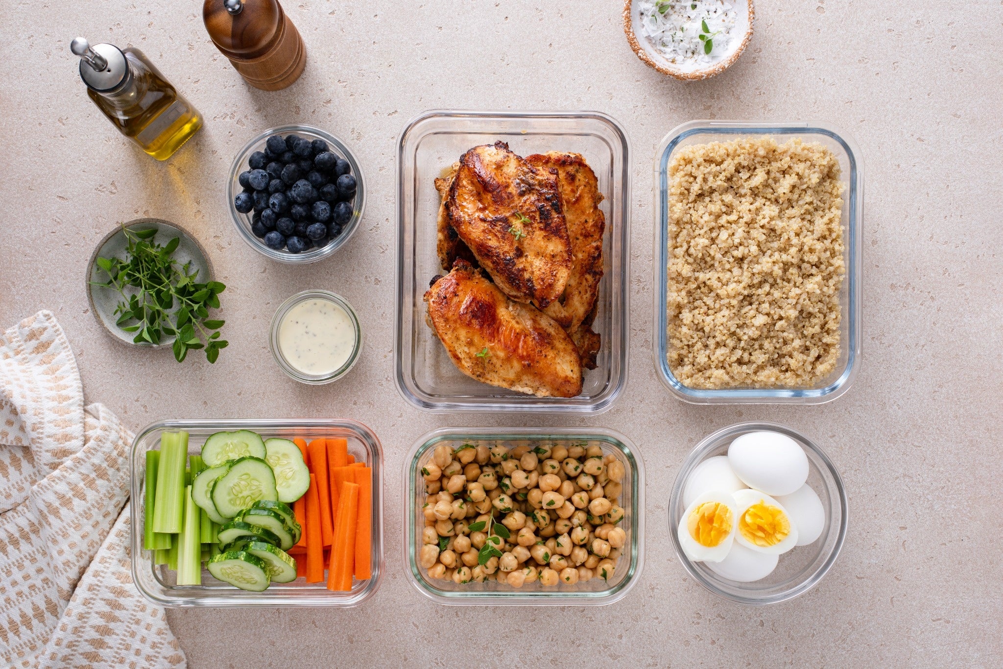 A variety of healthy meal prep ingredients arranged on a countertop, including grilled chicken, quinoa, vegetables, and blueberries.